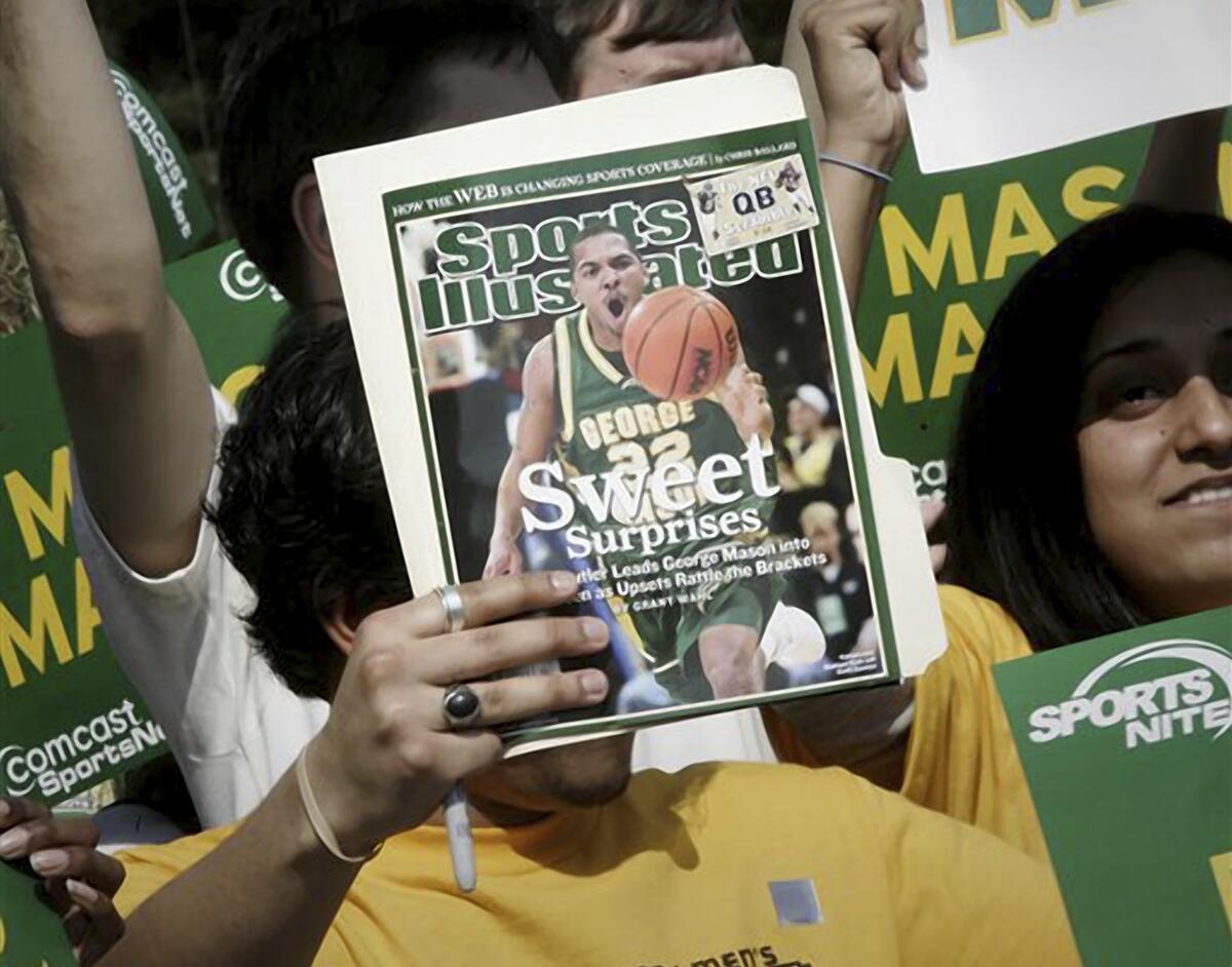 FILE - A George Mason University fan holds up a Sports Illustrated magazine at a send off for the team, March 29, 2006, in Fairfax, Va. Sports Illustrated is the latest media company damaged by being less than forthcoming about who or what is writing its stories. The website Futurism reported that the once-grand magazine used articles with authors who apparently don't exist, with photos generated by AI. The magazine denied claims that some articles themselves were AI-assisted, but has cut ties with a vendor it hired to produce the articles. (AP Photo/Lawrence Jackson, File)