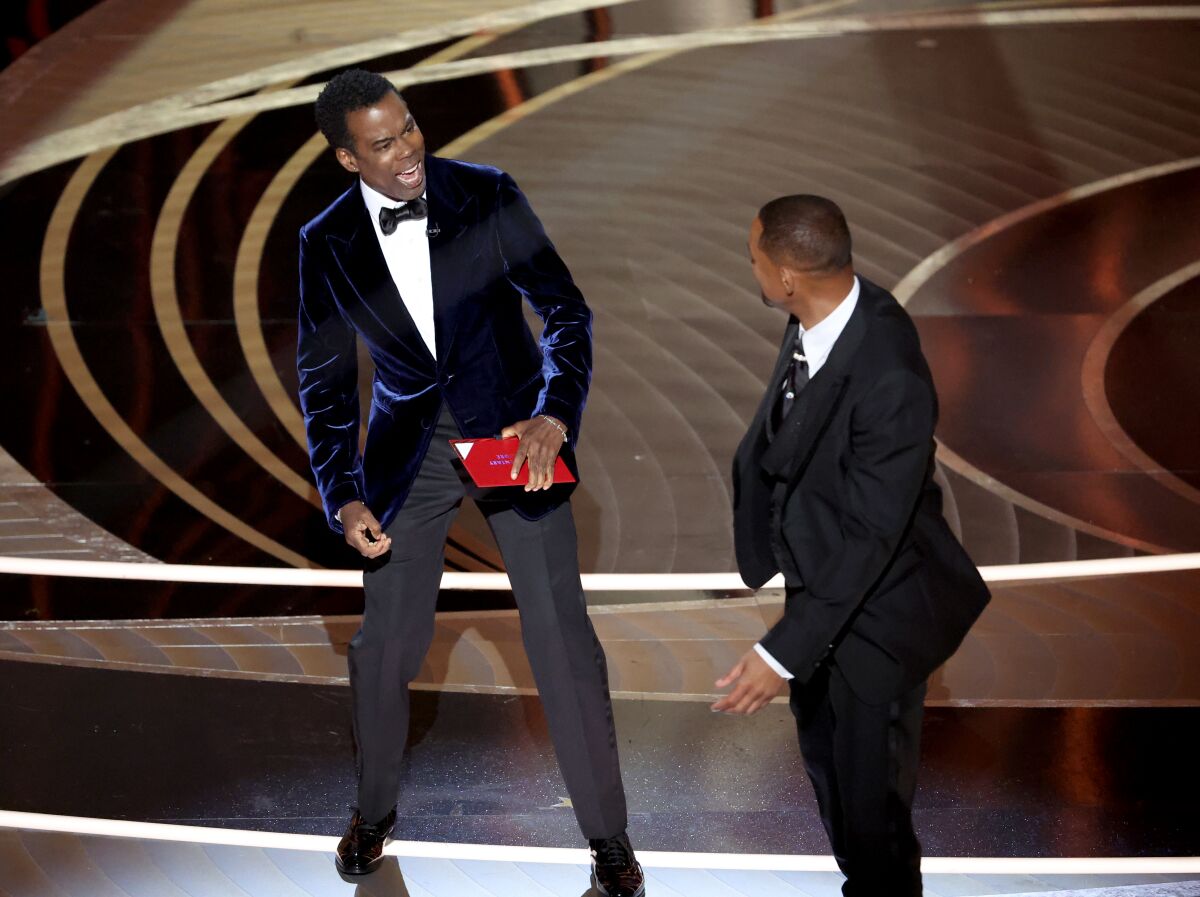 Two men in tuxes on a stage, one reacting to the other.