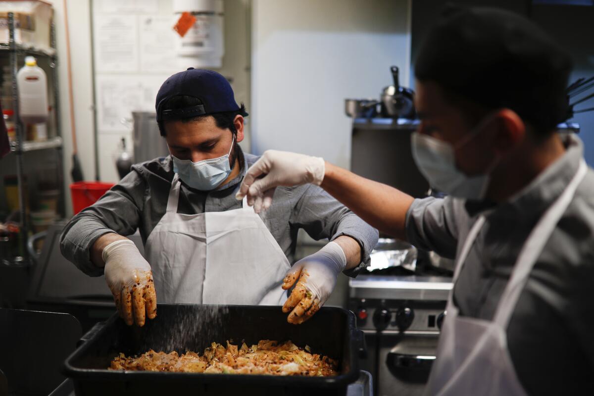 Kitchen worker Misael Cruz, 38, left, and Adam Rosas, 28, right, wear surgical masks and gloves as they prepare food