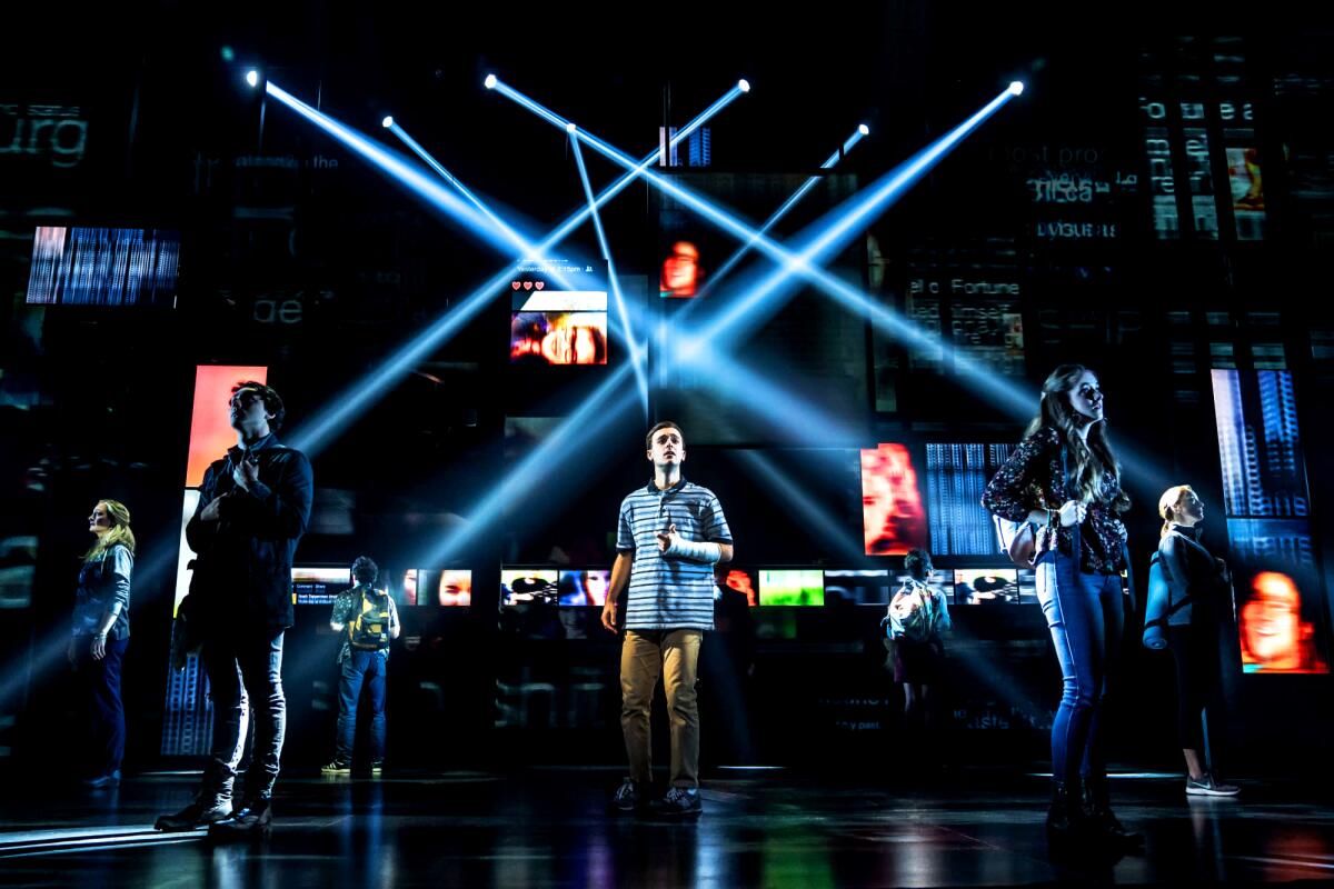 People stand on a dramatically lighted stage in "Dear Evan Hansen."