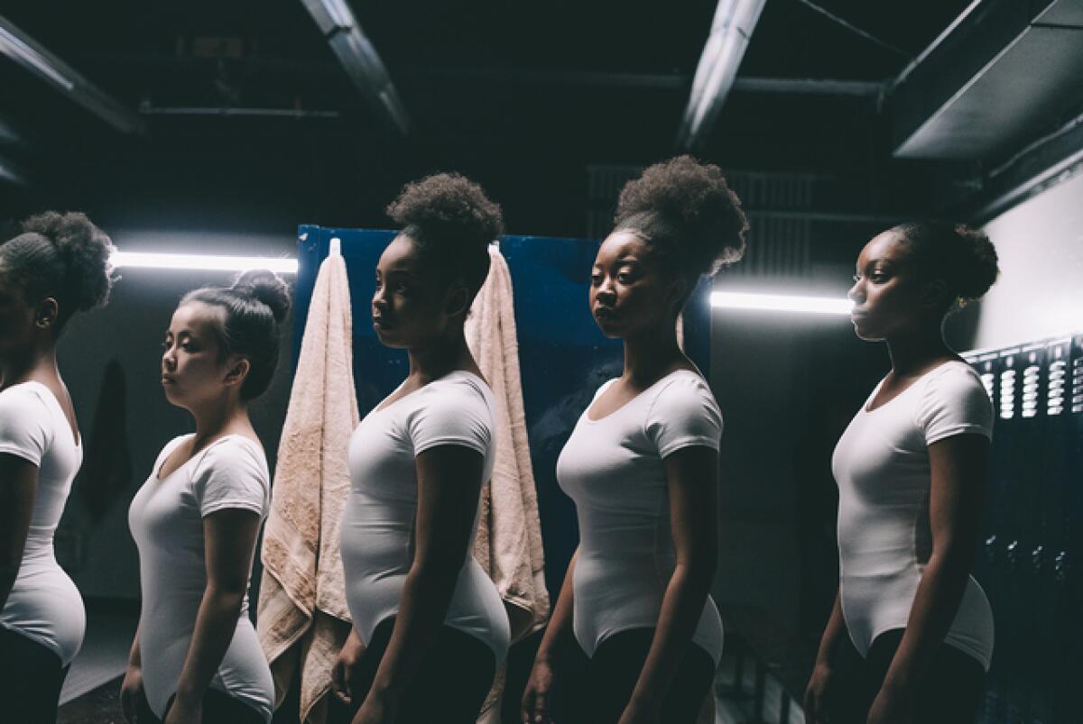 Five young women in gymnastics uniforms in a locker room