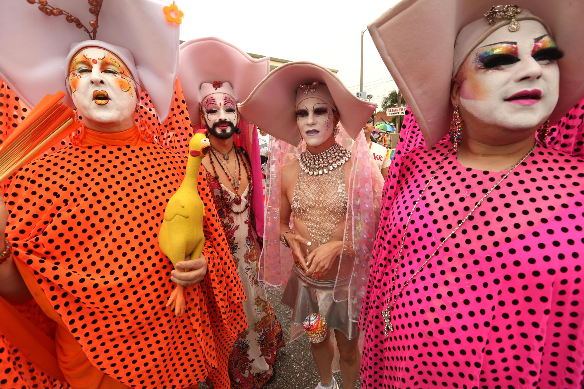 Drag nuns in white makeup and bright pink and orange gowns with black polka dots.
