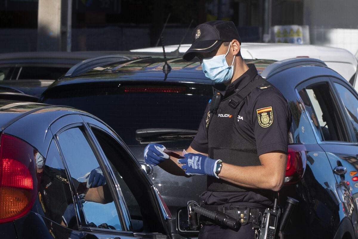 A police officer checks a driver's documents at a checkpoint on the outskirts of Madrid, Spain, Saturday, Oct. 3, 2020. Madrid is on a partial lockdown complying with an order from the Spanish government due to the high COVID-19 cases but determined to fight it in the courts. Measures that ban all nonessential trips in and out of the capital and nine of its suburbs, covering around 4.8 million people. (AP Photo/Paul White)