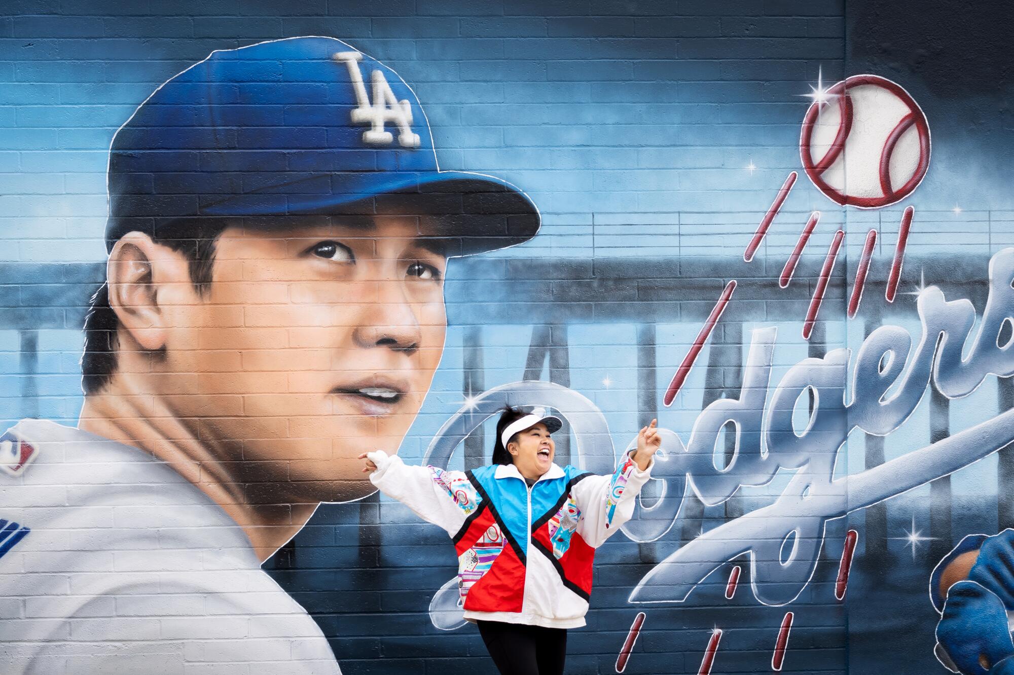 A smiling person dances in front of a mural showing Shohei Ohtani as a Dodger.