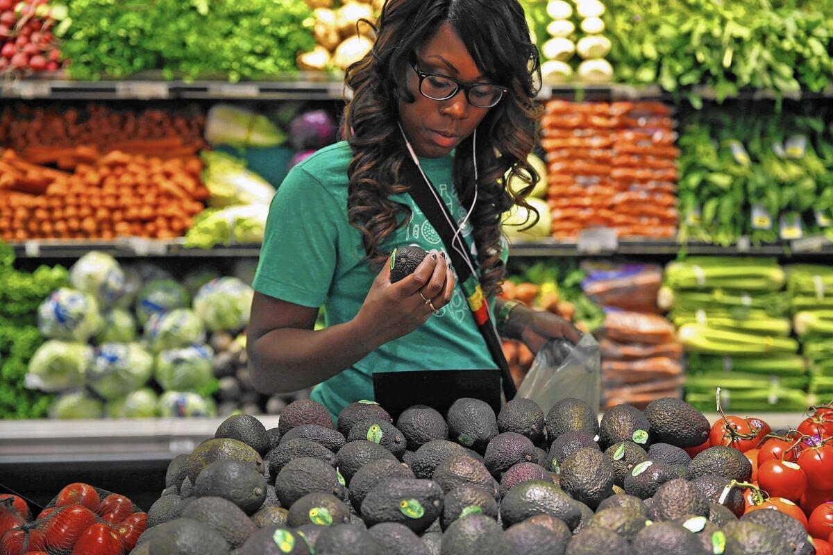 Instacart shopper Kara Pete looks over avocados at a Whole Foods Market in Sherman Oaks in September. Is it ethical to pay others to face coronavirus risks we'd rather avoid?