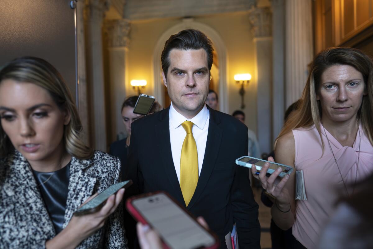 Rep. Matt Gaetz leaves the House chamber flanked by two people holding up phones.