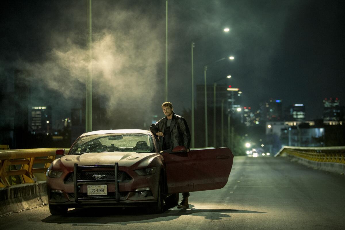 A man stands by his car on a smoky street.