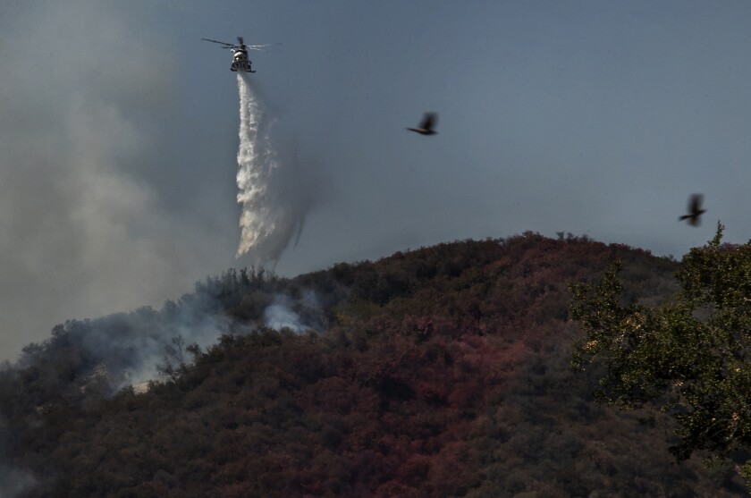 A helicopter drops water onto a wildfire