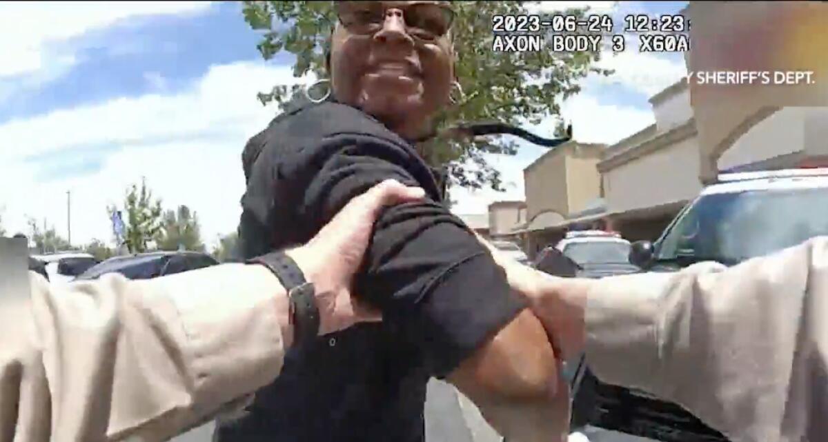 A police body camera image of a person looking back at the officer, whose arms reach forward to grab the person's upper arm