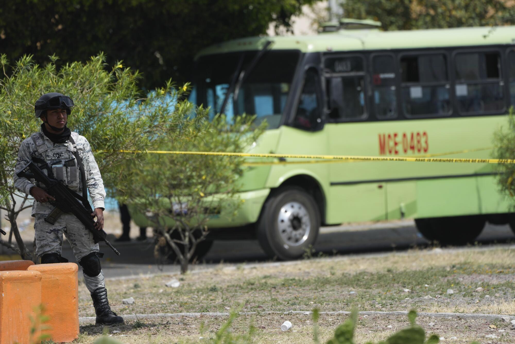 A member of the Mexican National Guard stands at the perimeter of a crime scene with a bus in the background.