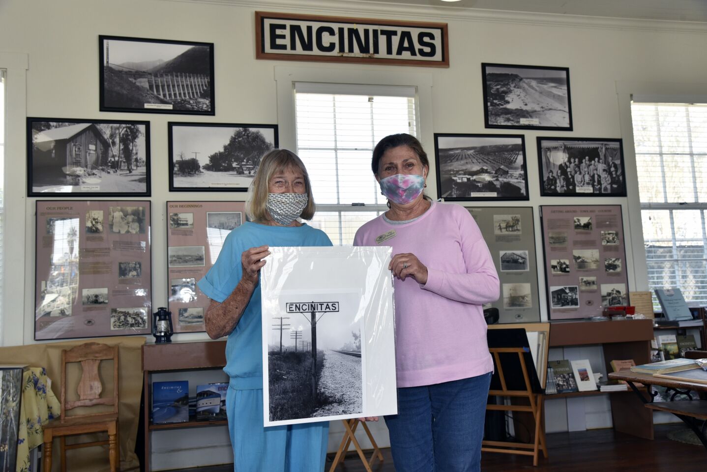 Pam Hammond Walker (great great grandaughter of schoolhouse builder EG Hammond) and Encinitas Historical Society Vice President Dana Donatelli hold a photo of a railroad sign that was recently added to the Society's collection