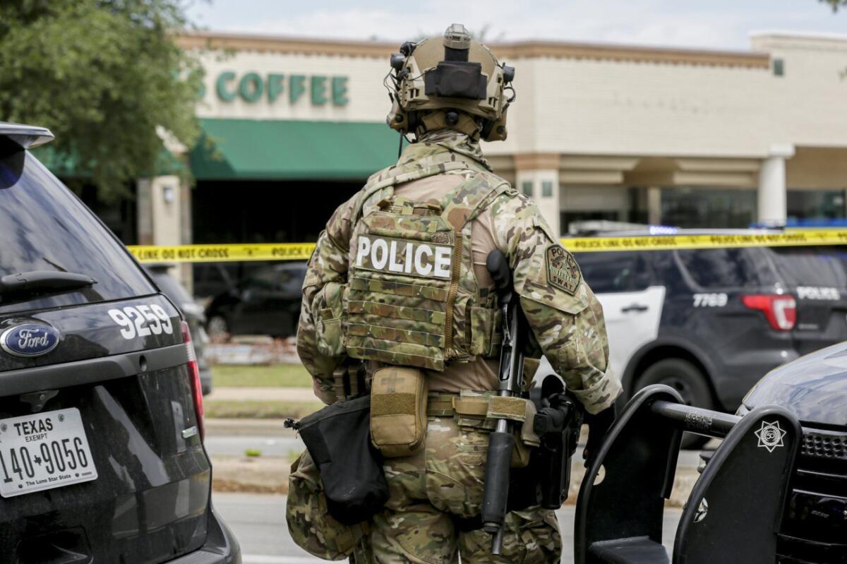 A heavily armed officer in camouflage stands outside a shopping center.
