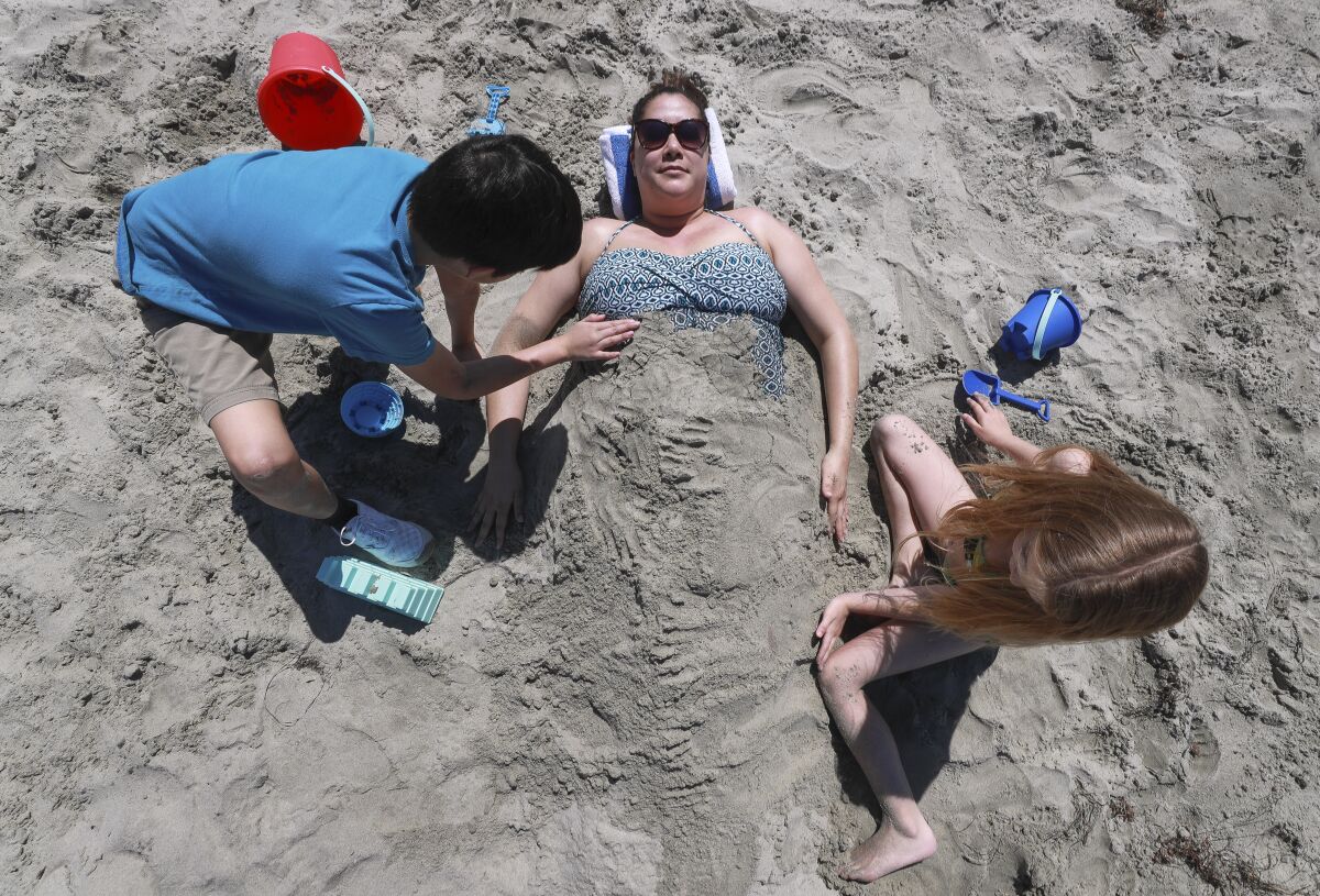 Sophia Balangue is covered with sand by son Liam, 8, and friend Riley Sunblad, 7, during a pre-restrictions March visit to Oceanside City Beach.