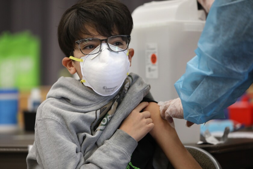 A boy in a mask and glasses rolls his sleeve up for a vaccine shot