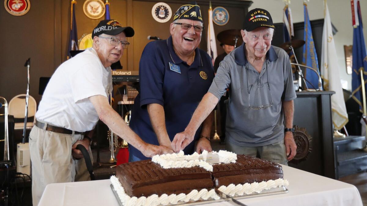 Doug Nye, center, commander of American Legion Newport Harbor Post 291, cuts a cake with World War II veteran Leander Kelter, left, of Huntington Beach and Korean War veteran Warren Morris of Orange during a luncheon Thursday celebrating the American Legion’s 99th anniversary.