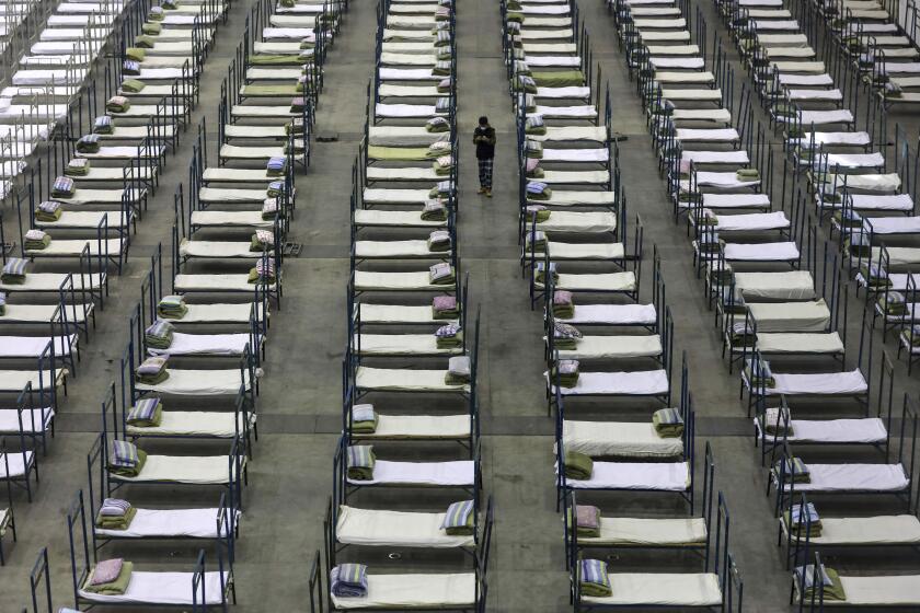 FILE - In this Feb. 4, 2020, file photo, a worker walks among beds in a convention center that has been converted into a temporary hospital in Wuhan in central China's Hubei Province. The virus outbreak that began in China and has spread to more than 20 countries is stretching already-strained public health systems in Asia and beyond, raising questions over whether everyone can get equal access to treatment. (Chinatopix via AP, File)
