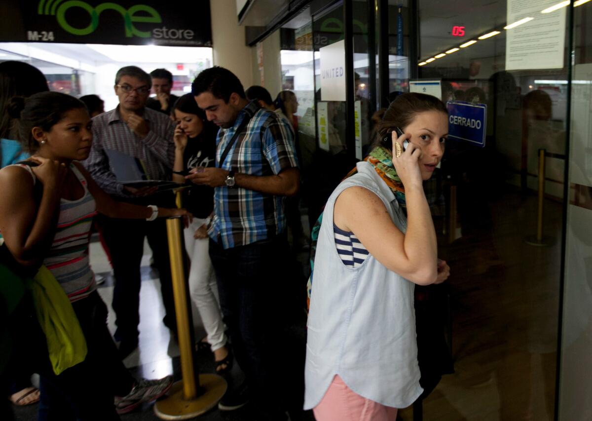 A woman speaks on her phone as she seeks information about flight sales outside a closed United Airlines office in Caracas, Venezuela. Some airlines have suspended ticket sales transacted in bolivars, the local currency, until the government pays money it owes the carriers.