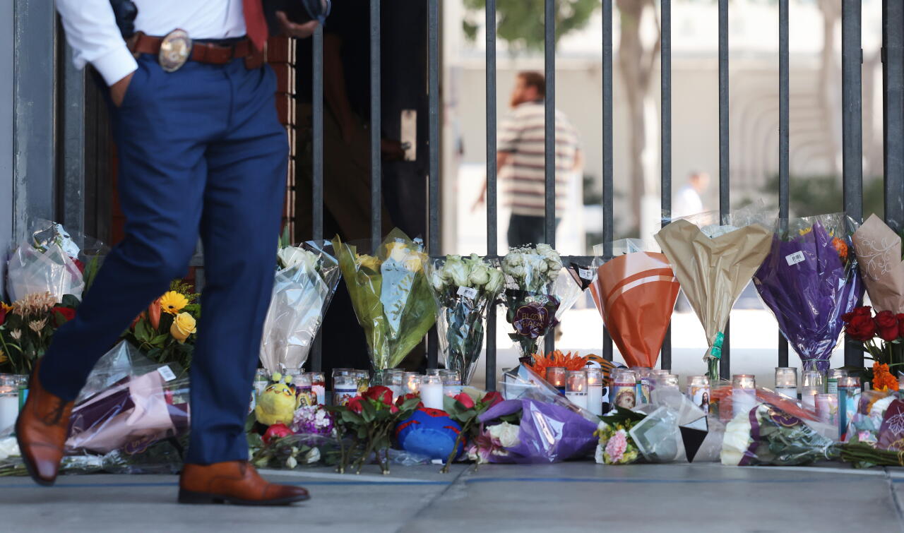 A person with a law enforcement badge walks past a row of flower bouquets and lighted candles