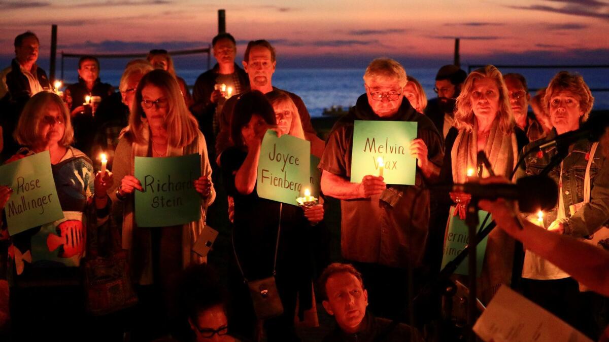 Participants hold signs and sing traditional jewish songs during a candlelight vigil in honor of the Pittsburgh synagogue shooting victims at Laguna Beach's Main Beach Sunday night.