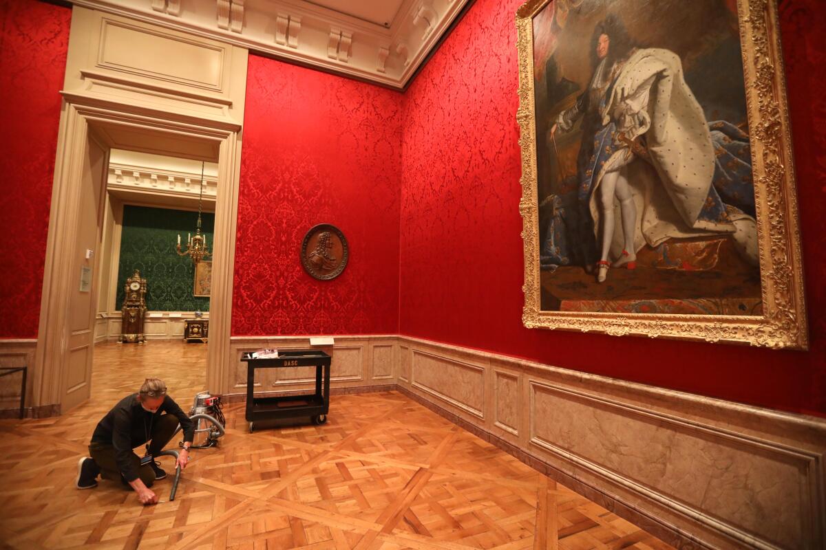 A woman bends to use a vacuum beneath the watchful eye of a portrait