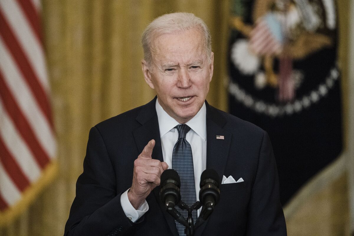 A man in suit and tie, speaking before microphones, gestures to make a point