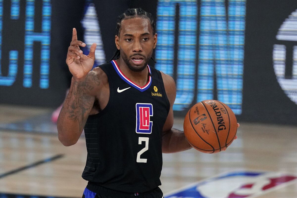 Clippers forward Kawhi Leonard raises one hand while holding the ball with his other hand on the court.