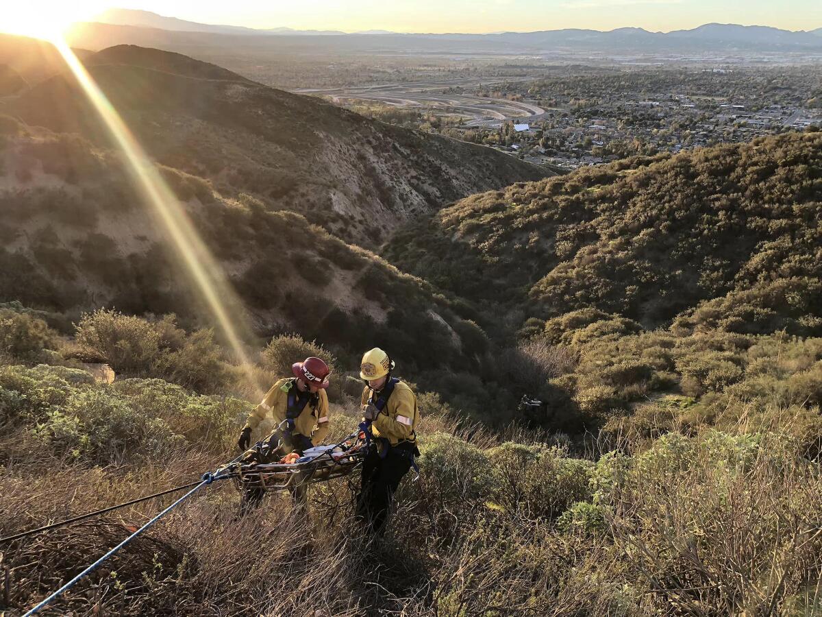 Rescue personnel wearing helmets carrey a gurney on a dry mountainside 