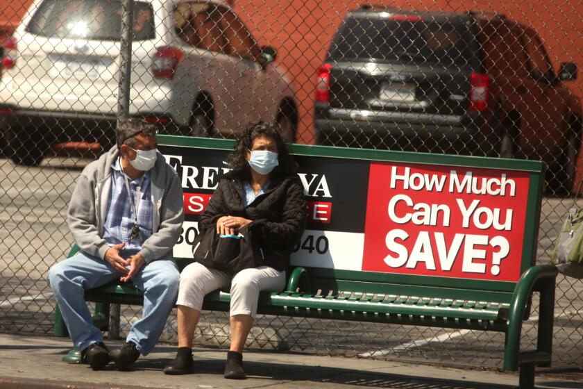 LOS ANGELES, CA - APRIL 14, 2020 - A couple heed a pointed question of a nearby advertisement and know the value of wearing a mask during the coronavirus pandemic along Vermont Avenue in Los Angeles on Tuesday, April 14, 2020. (Genaro Molina / Los Angeles Times)