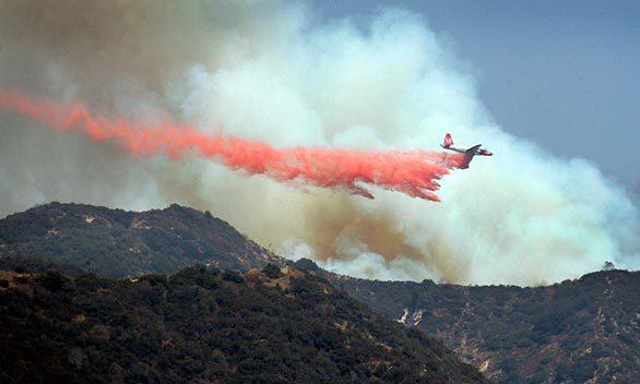 An airplane drops fire retardant Thursday afternoon in the Angeles National Forest in a view from Foothill Boulevard in La Cresenta. With temperatures hovering near 100 degrees, firefighters are trying to contain flames racing through dry brush in the forest north of the foothill community of La Canada Flintridge.