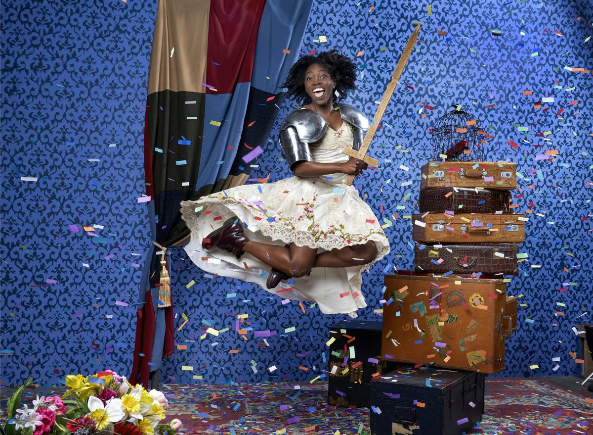 A woman in costume leaps into the air on a stage amid confetti.