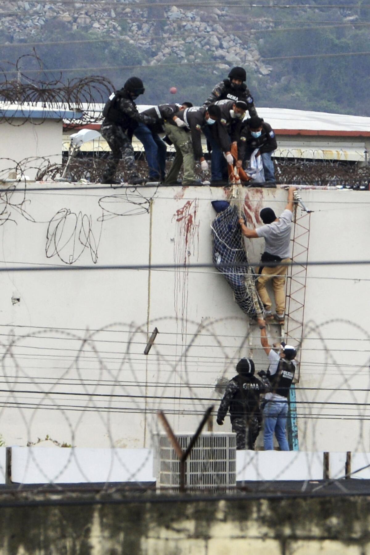 Police lower the body of an inmate, wrapped in a shroud, from the roof of the Litoral Penitentiary