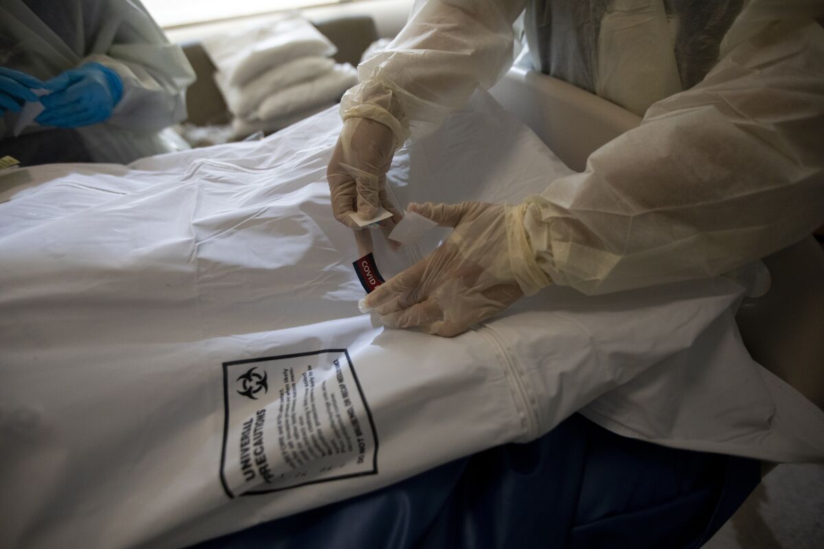 Nurses place a "covid patient" label and covid stickers on the white bag containing a deceased patient