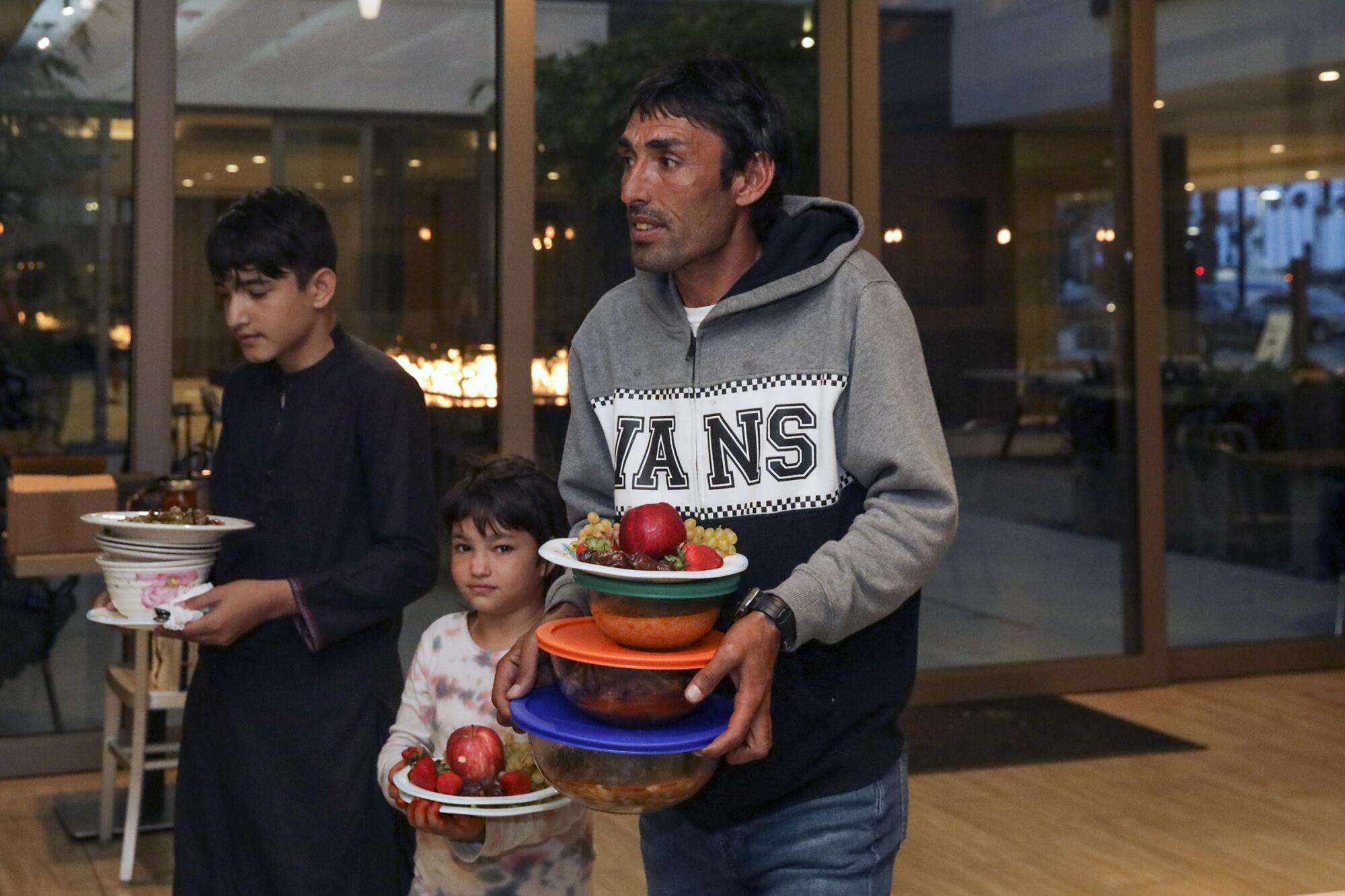 A man and two children hold plates and containers of food.
