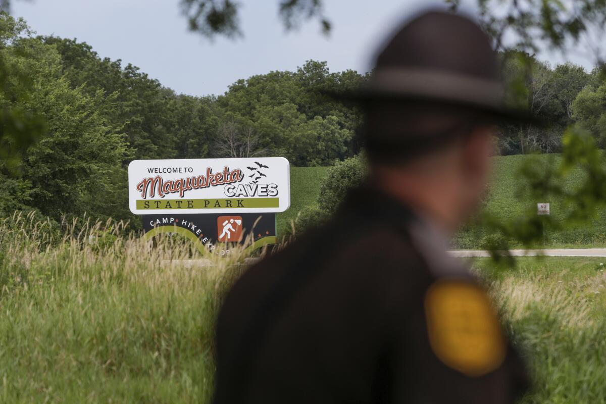 A fuzzy image in foreground of a state trooper with a sign in background reading 'Welcome to Maquoketa Caves State Park'