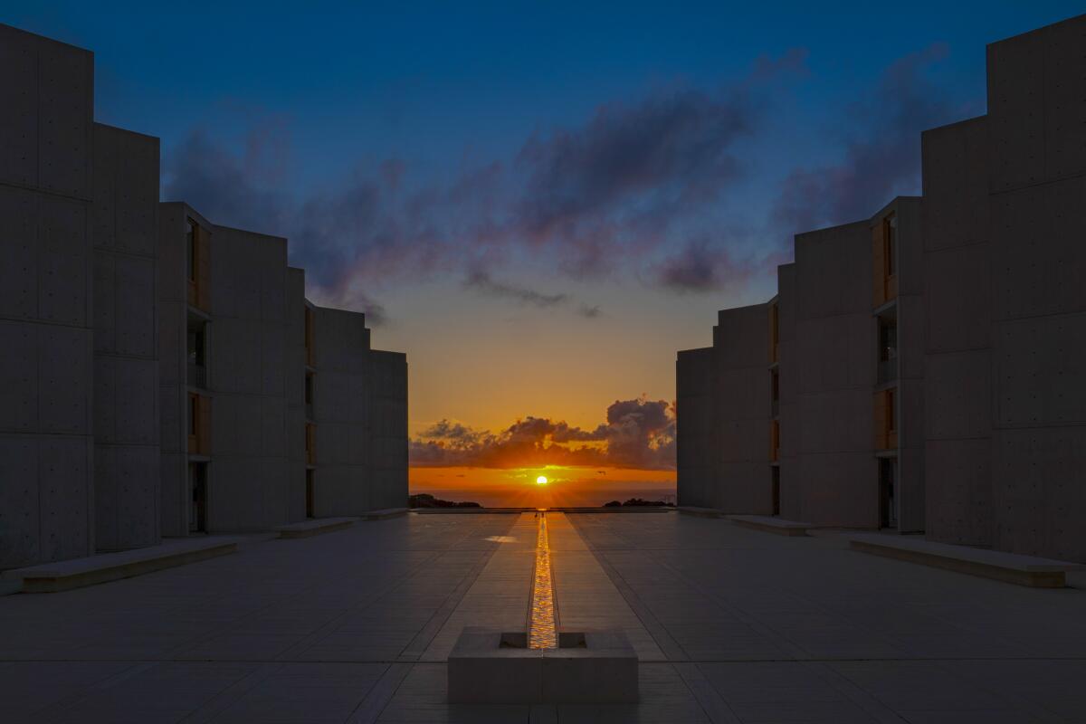 The setting sun lines up with and illuminates a channel of water in an open plaza at the Salk Institute. 