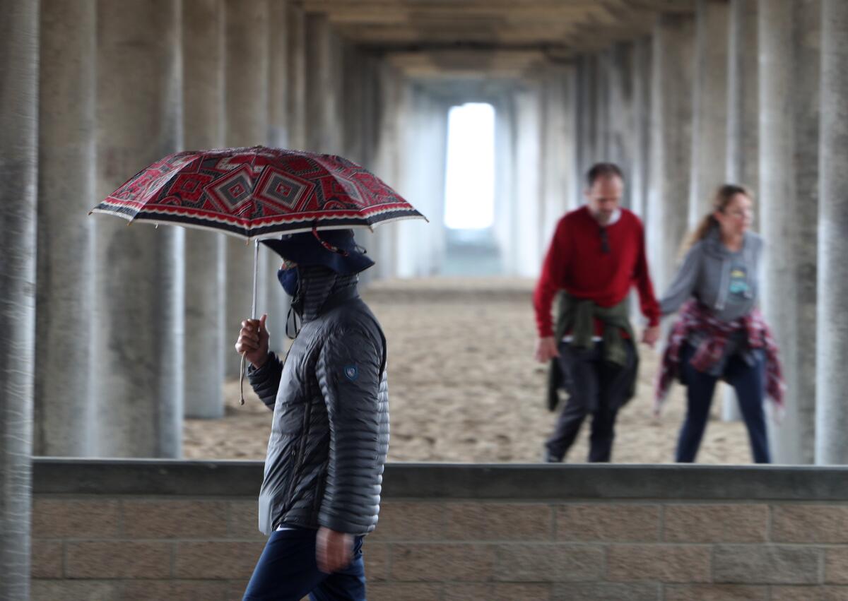  People walk under the Huntington Beach pier in light rain