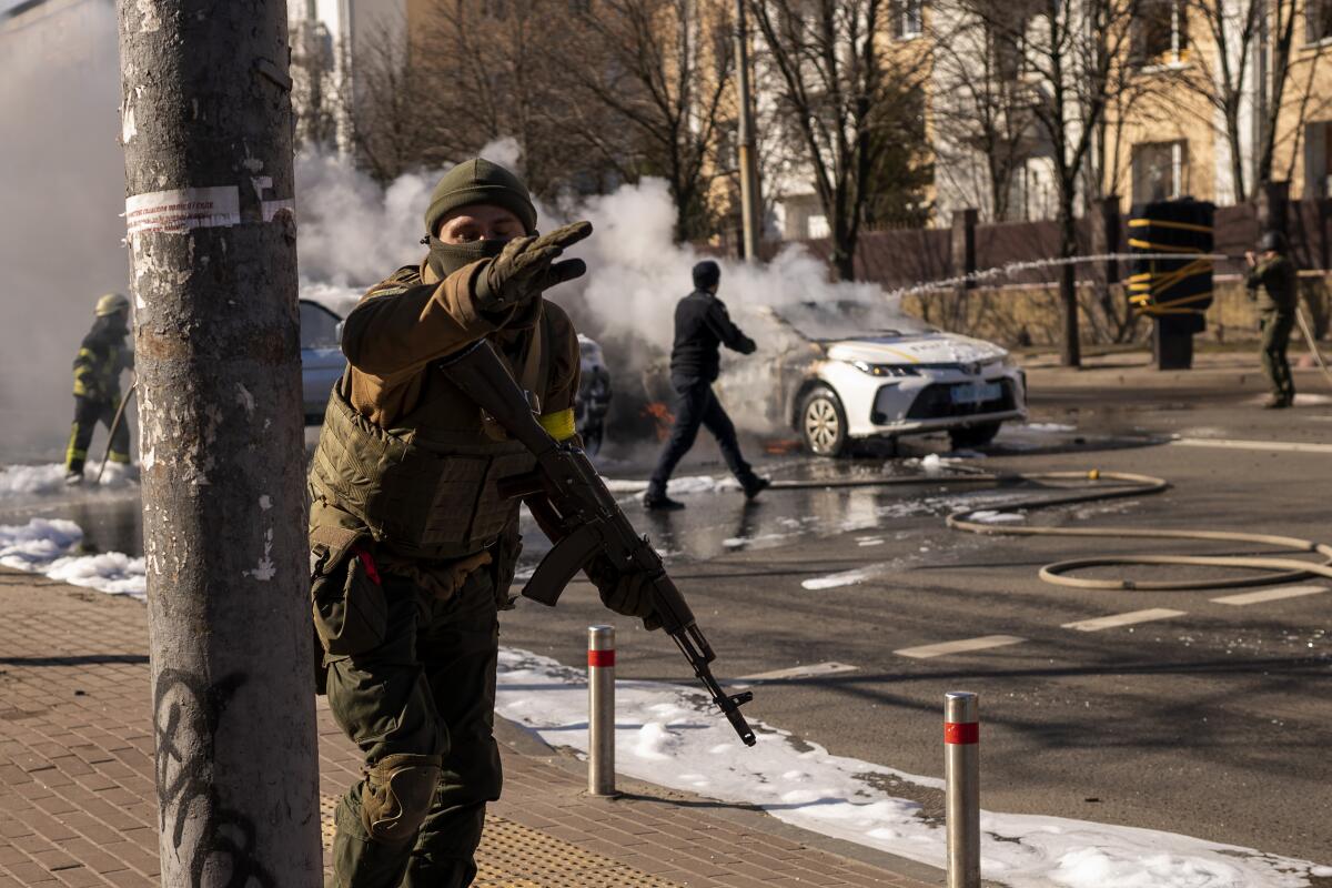 Ukrainian soldiers take positions outside a military facility as two cars burn, in a street in Kyiv, Ukraine