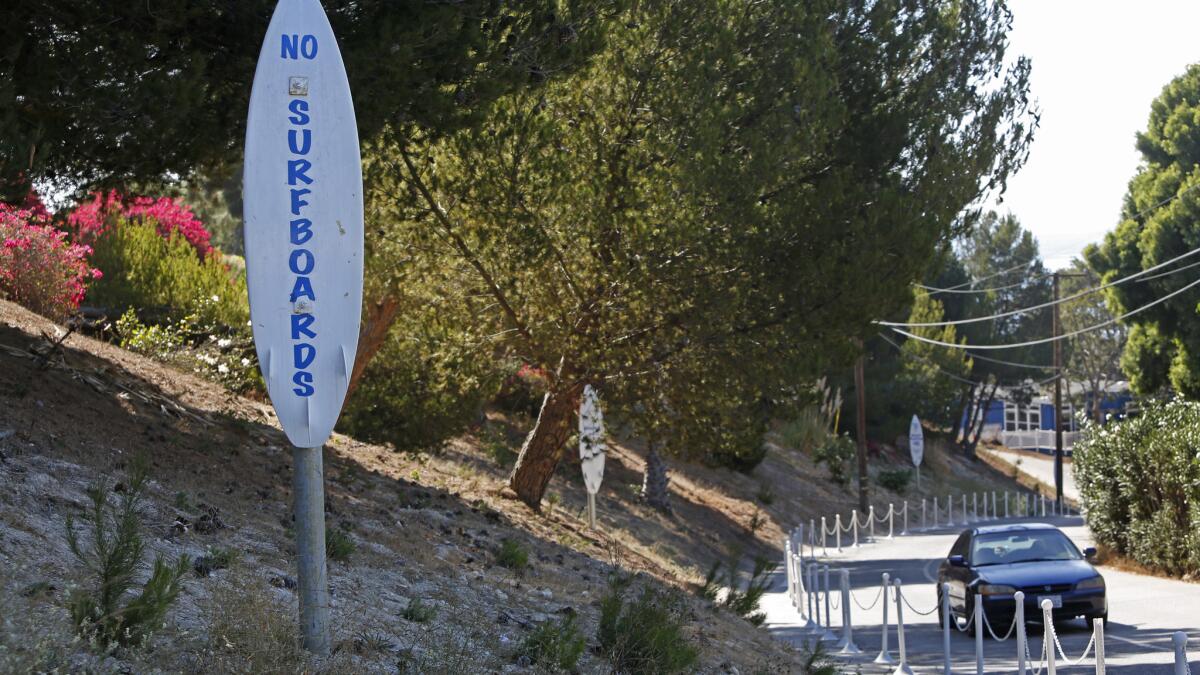 A "no surfboards" warning sign is posted along Paradise Cove Road, which leads to Paradise Cove in Malibu. The cove's owner has agreed to take down such signs.