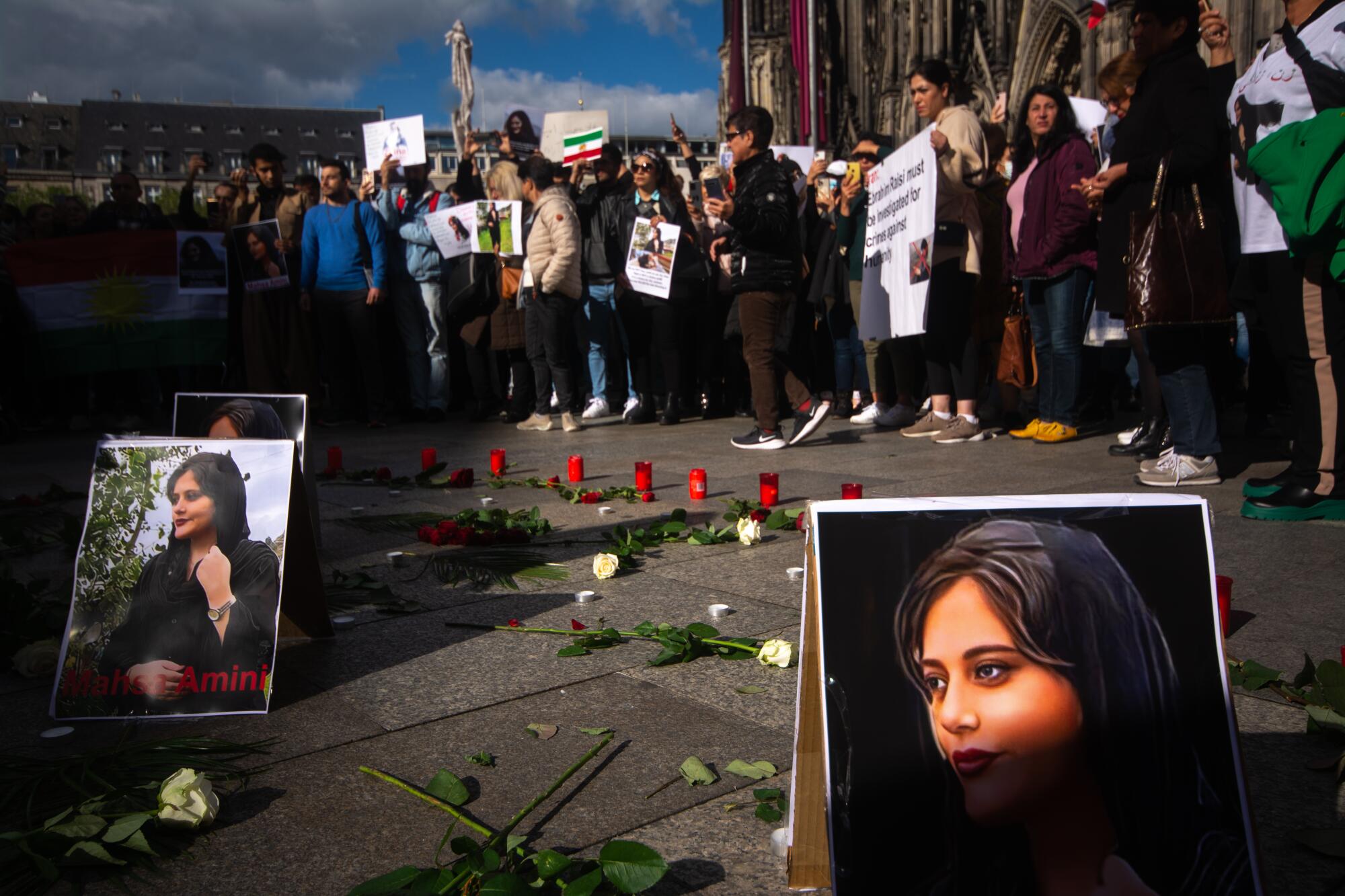 People gather in front of Dom Cathedral in Cologne, Germany, amid votive candles and posters of  