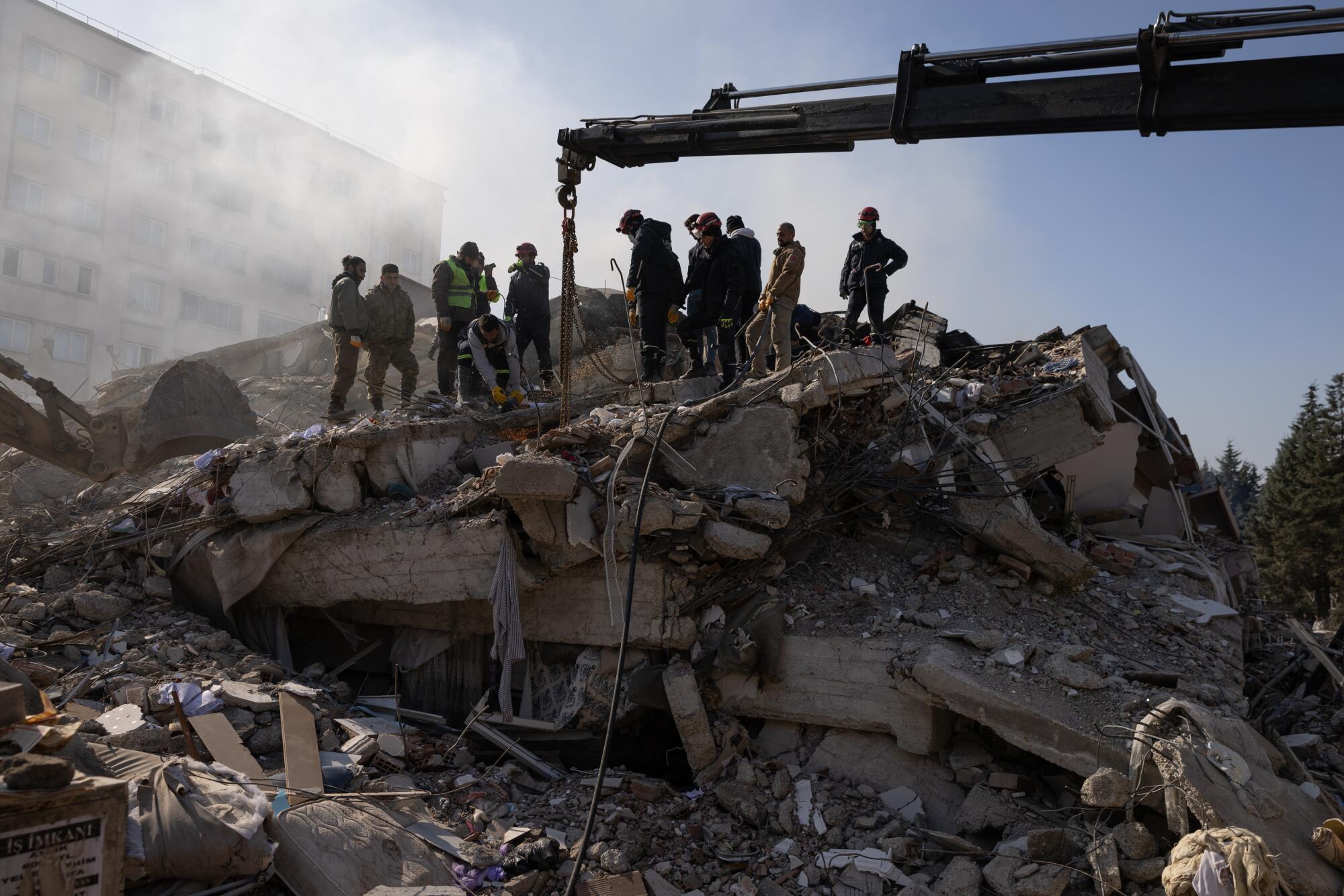 Several people standing and one kneeling on top of a large pile of rubble near a crane