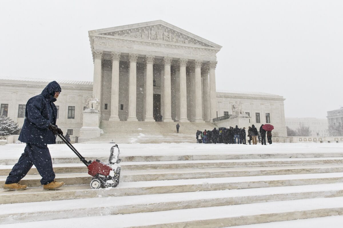 A worker clears snow from the plaza at the Supreme Court in Washington on March 3 as those waiting to hear oral arguments line up.