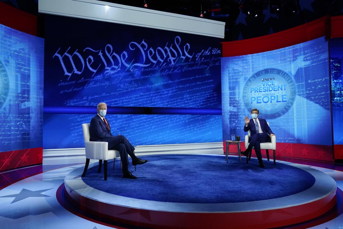 Democratic presidential candidate Joe Biden and ABC News anchor George Stephanopoulos sit on stage, masked, for a town hall.