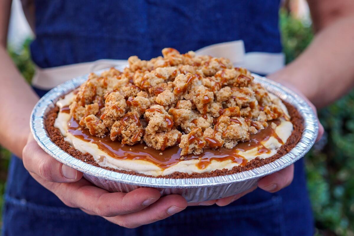 A crumble-and-caramel-topped ice cream pie in a pie tin held out by two hands.