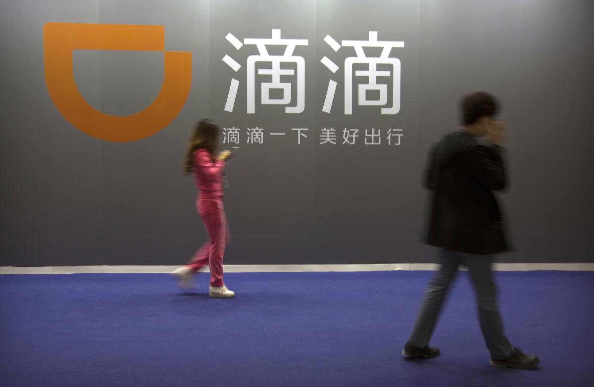 Two people walk past a sign for Chinese ride-hailing service Didi Chuxing in Beijing.
