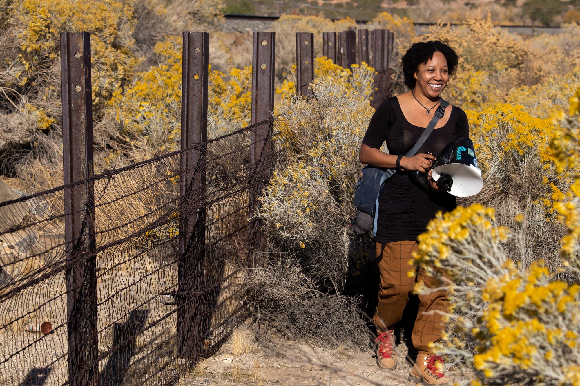 A woman standing next to a fence among boulders and fading rabbit bush blooms.