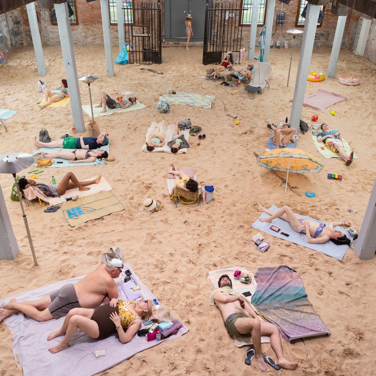 People lie on beach towels in the sand.