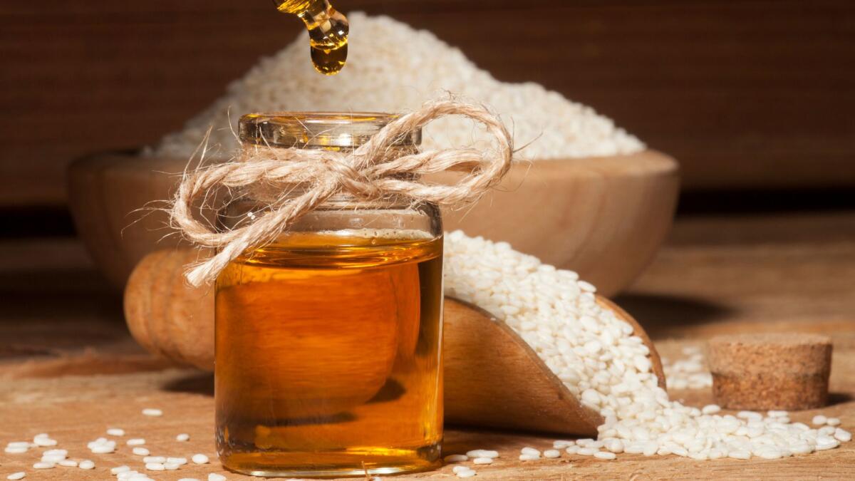 Fresh sesame oil in a glass bottle and seeds in wooden bowl and spoon on wooden background