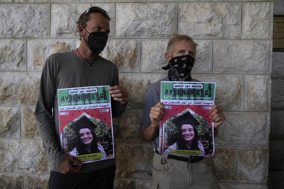 Two people wearing face masks hold up posters with the image of a young woman wearing a graduation cap.