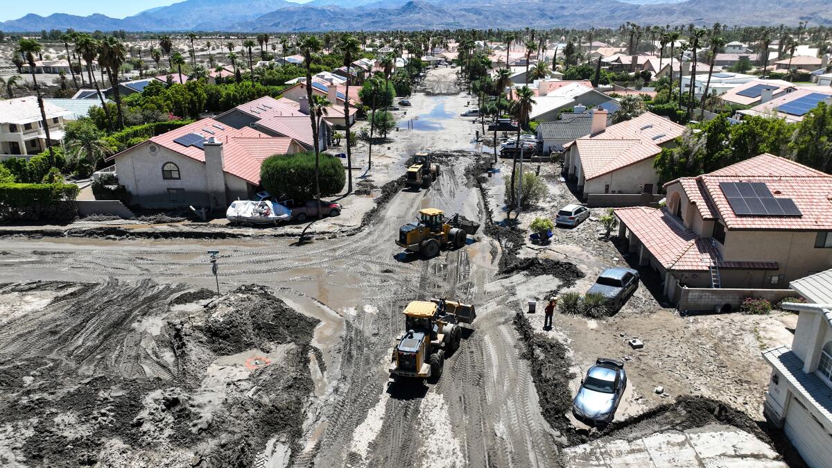 Construction vehicles at work in muddy roads in a neighborhood after flooding.