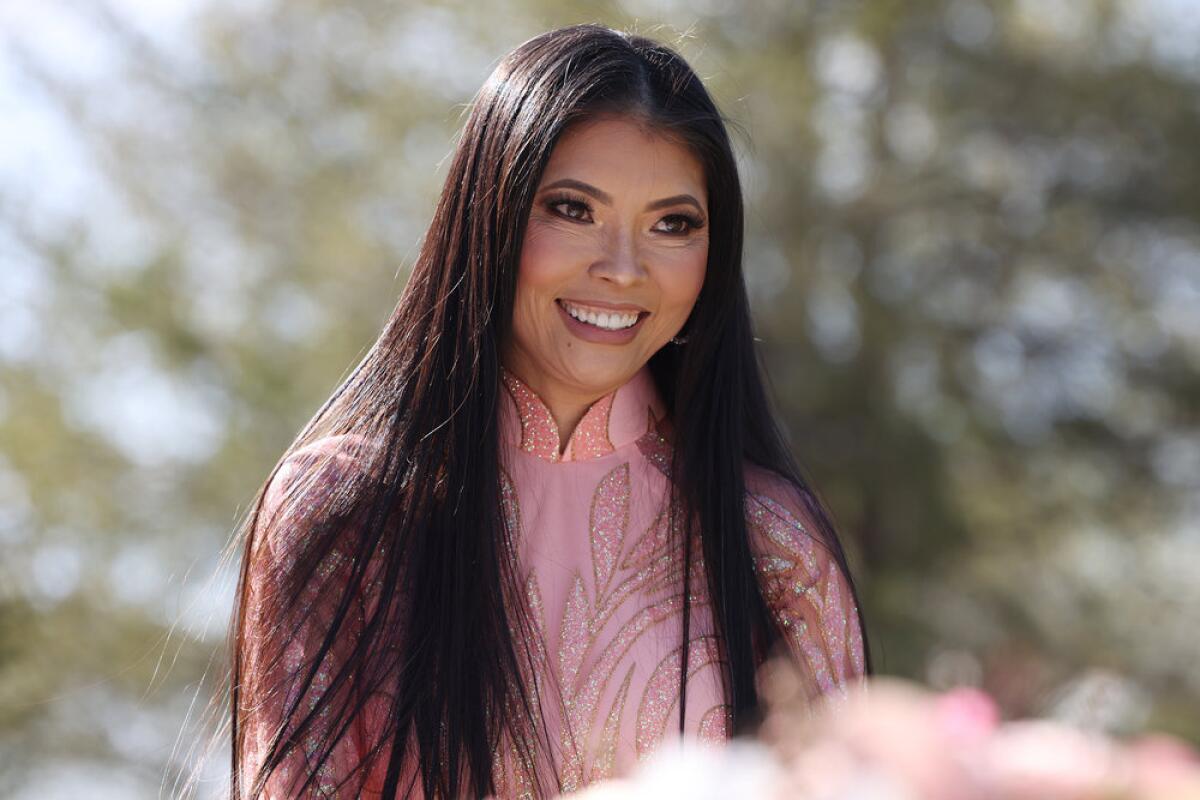 Jennie Nguyen with long hair in a garden wearing a pink top and smiling.